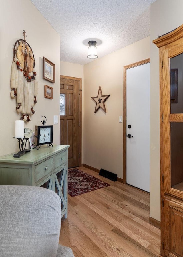 foyer entrance with baseboards, a textured ceiling, and light wood finished floors