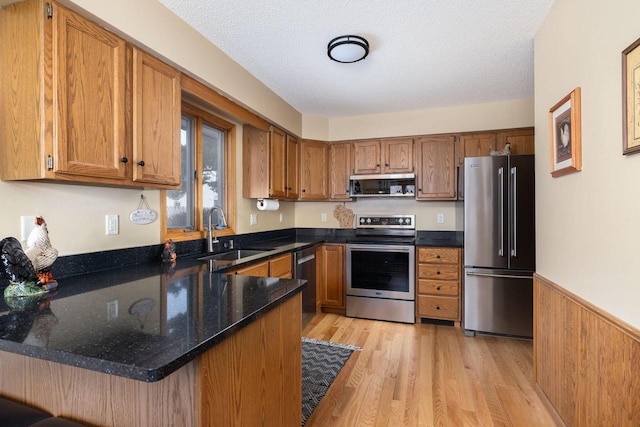 kitchen featuring a peninsula, appliances with stainless steel finishes, brown cabinets, and a sink