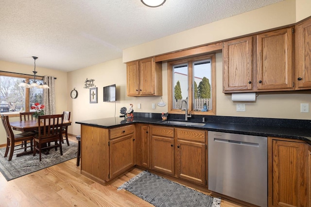 kitchen featuring a peninsula, a sink, stainless steel dishwasher, light wood-type flooring, and brown cabinetry