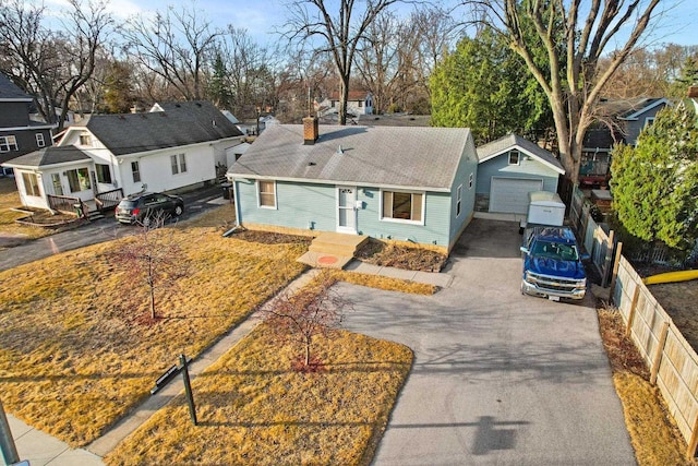 view of front facade featuring fence, a detached garage, a shingled roof, a chimney, and aphalt driveway