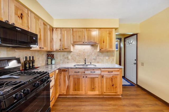 kitchen with wood finished floors, light stone countertops, a sink, black appliances, and tasteful backsplash