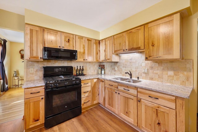 kitchen with light stone counters, black appliances, light wood-style floors, and a sink