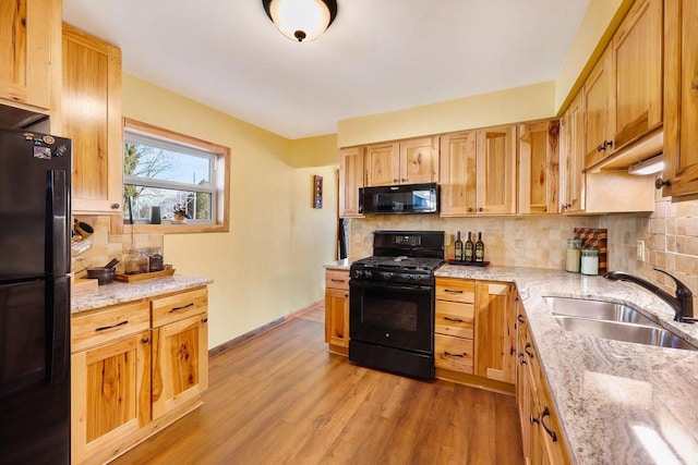 kitchen featuring black appliances, light wood-style flooring, a sink, tasteful backsplash, and baseboards