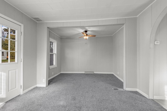 carpeted empty room featuring arched walkways, ornamental molding, visible vents, and a ceiling fan