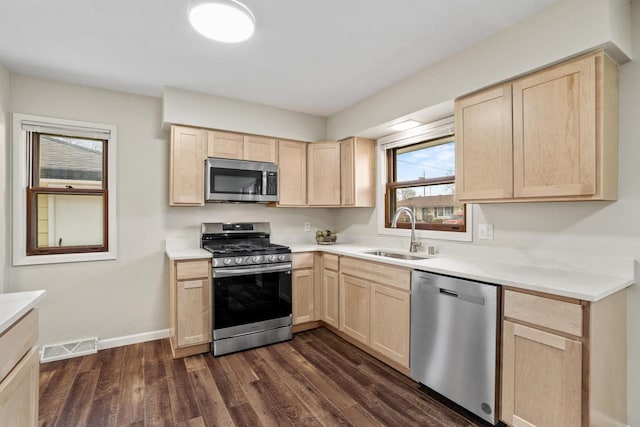 kitchen featuring light brown cabinets, appliances with stainless steel finishes, dark wood-type flooring, and a sink