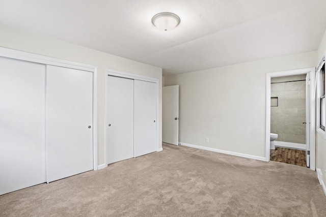 unfurnished bedroom featuring baseboards, carpet floors, ensuite bath, and multiple closets