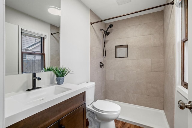 full bathroom featuring toilet, wood finished floors, tiled shower, and vanity