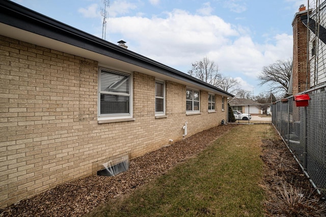 view of side of home with crawl space, brick siding, a lawn, and fence