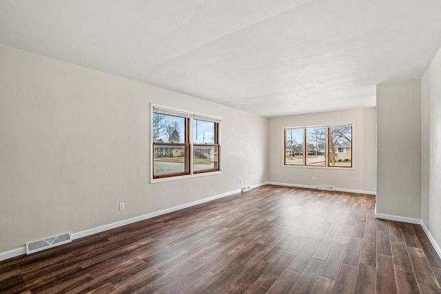 spare room with dark wood finished floors, visible vents, and baseboards