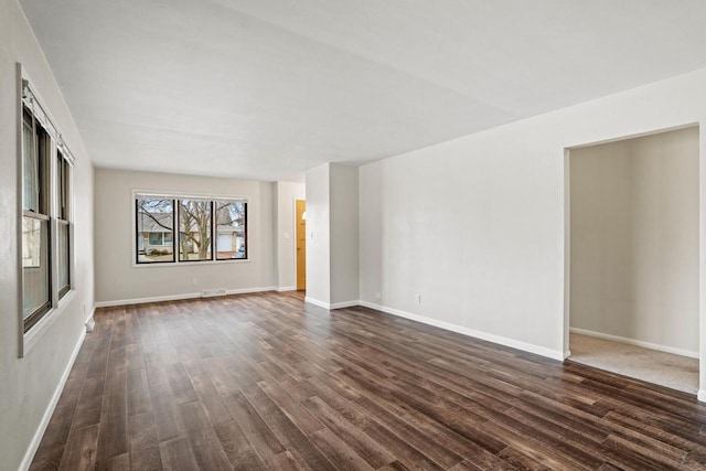 empty room with dark wood-style floors, visible vents, and baseboards