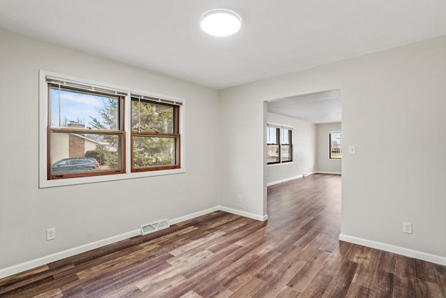 empty room featuring wood finished floors, visible vents, and baseboards