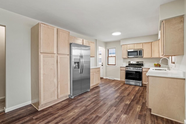 kitchen featuring light brown cabinets, appliances with stainless steel finishes, dark wood finished floors, and a sink