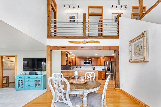 dining area featuring light wood-style floors, baseboards, and a high ceiling