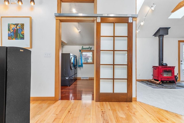 hallway featuring rail lighting, wood-type flooring, baseboards, and washer and clothes dryer