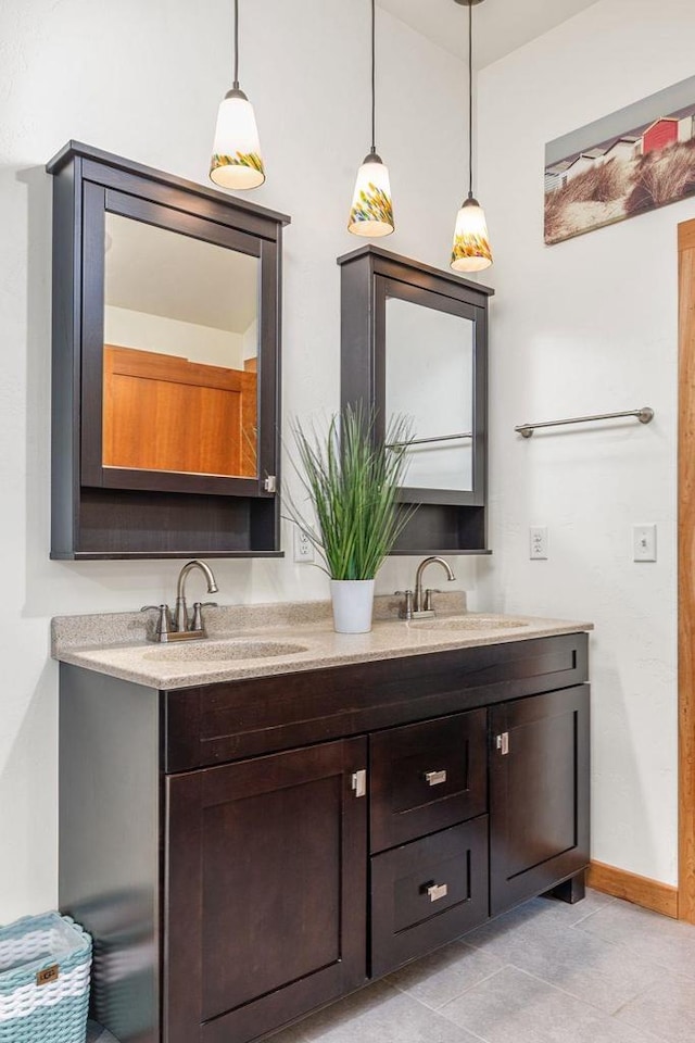 full bathroom with double vanity, tile patterned flooring, a sink, and baseboards