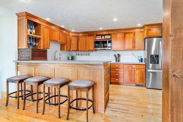 kitchen with appliances with stainless steel finishes, light wood-type flooring, a breakfast bar, and tasteful backsplash