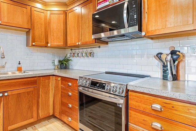 kitchen with stainless steel appliances, a sink, light countertops, brown cabinets, and tasteful backsplash