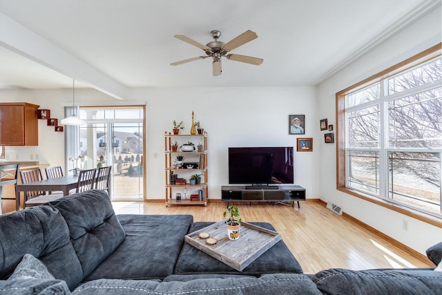 living area with visible vents, light wood-style flooring, a ceiling fan, and baseboards