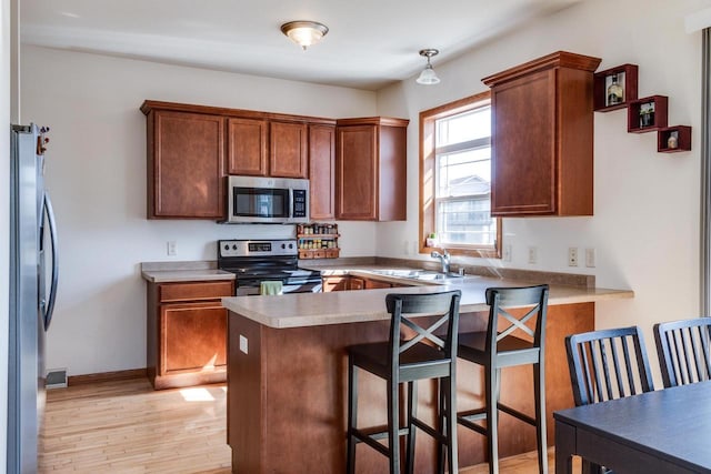 kitchen featuring light wood-type flooring, a sink, stainless steel appliances, a peninsula, and light countertops