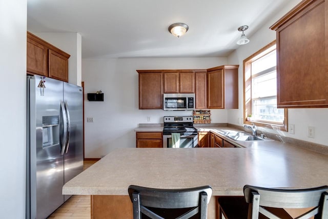 kitchen featuring a breakfast bar, a sink, stainless steel appliances, a peninsula, and brown cabinetry