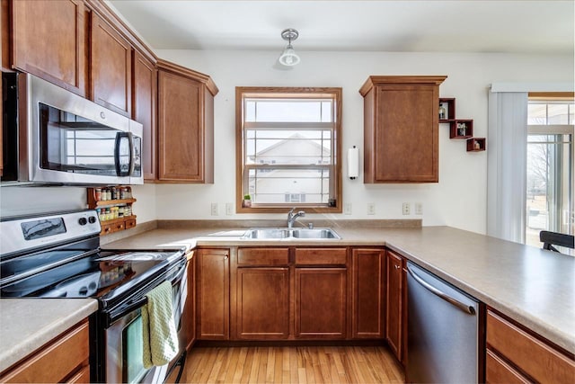 kitchen featuring light wood finished floors, appliances with stainless steel finishes, brown cabinetry, and a sink