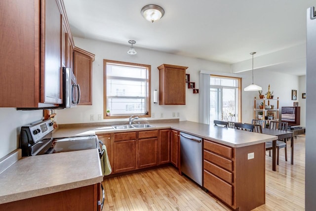 kitchen featuring brown cabinetry, a peninsula, stainless steel appliances, light wood-style floors, and decorative light fixtures