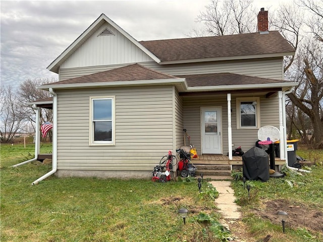 view of front facade featuring covered porch, a front lawn, roof with shingles, and a chimney