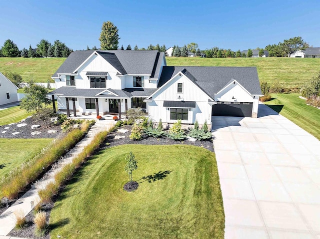 modern farmhouse style home with concrete driveway, roof with shingles, an attached garage, board and batten siding, and a front yard