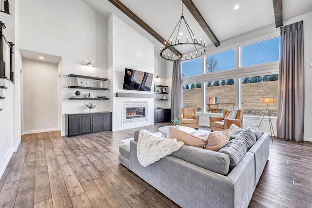 living room featuring beam ceiling, a towering ceiling, a tiled fireplace, and wood finished floors