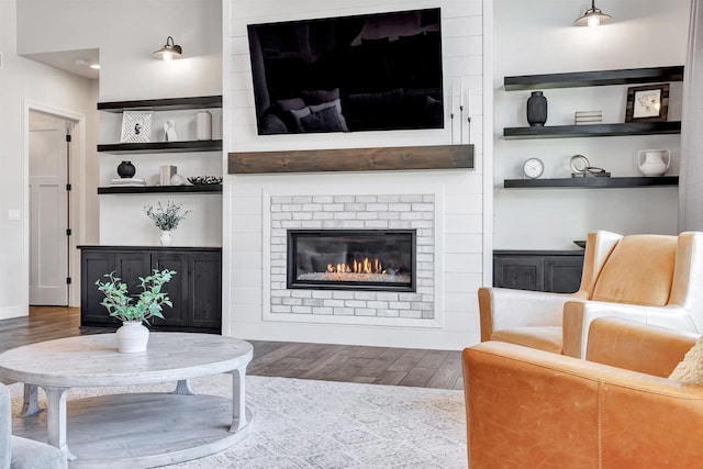 living room featuring built in features, a large fireplace, and wood finished floors