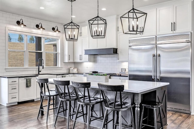 kitchen featuring built in fridge, under cabinet range hood, wood finished floors, a center island, and tasteful backsplash