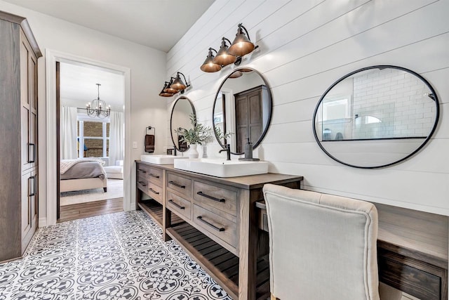 ensuite bathroom featuring connected bathroom, a notable chandelier, wood walls, a sink, and double vanity