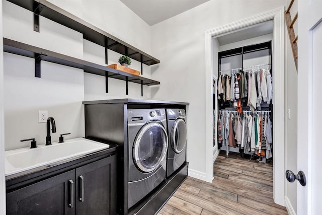 clothes washing area featuring a sink, baseboards, light wood-style floors, cabinet space, and washer and clothes dryer