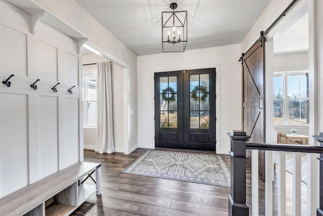 mudroom with french doors, dark wood finished floors, a barn door, a chandelier, and baseboards