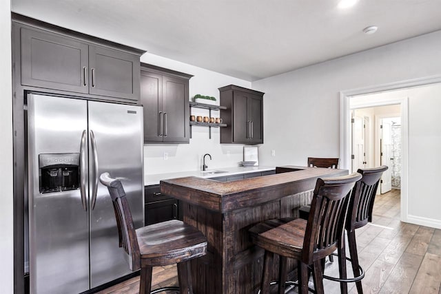 kitchen featuring dark brown cabinetry, a sink, light countertops, light wood-type flooring, and stainless steel fridge with ice dispenser