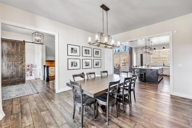 dining area featuring a chandelier, a barn door, dark wood-type flooring, and baseboards