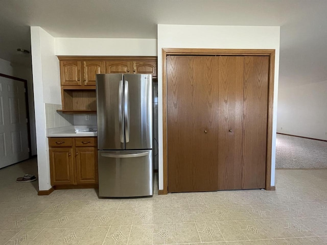 kitchen featuring brown cabinetry, freestanding refrigerator, light countertops, and open shelves