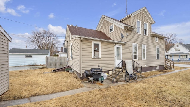 rear view of property with entry steps, roof with shingles, and fence