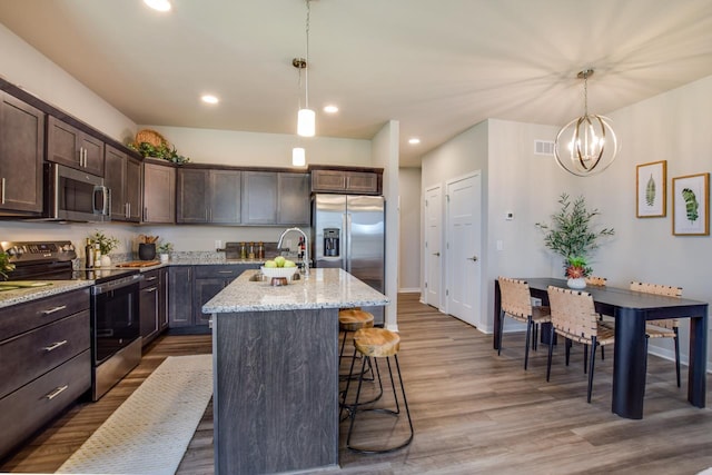 kitchen featuring wood finished floors, appliances with stainless steel finishes, a sink, dark brown cabinets, and light stone countertops