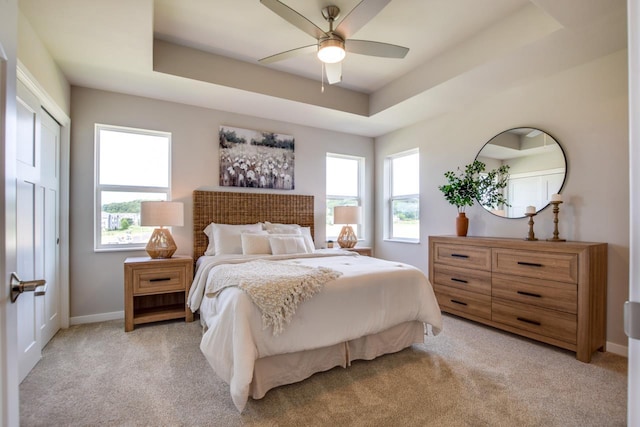 bedroom featuring a tray ceiling, light carpet, ceiling fan, and baseboards