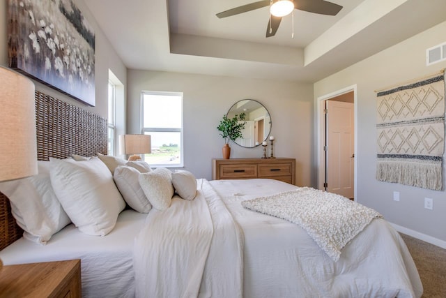 carpeted bedroom featuring ceiling fan, a raised ceiling, visible vents, and baseboards