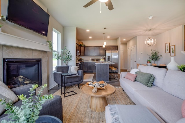 living room with recessed lighting, ceiling fan with notable chandelier, baseboards, light wood finished floors, and a tiled fireplace