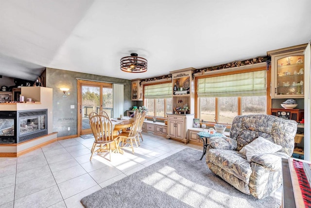 dining space featuring light tile patterned floors, baseboards, and a multi sided fireplace