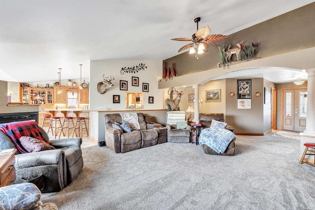 living area with arched walkways, a ceiling fan, vaulted ceiling, carpet, and decorative columns