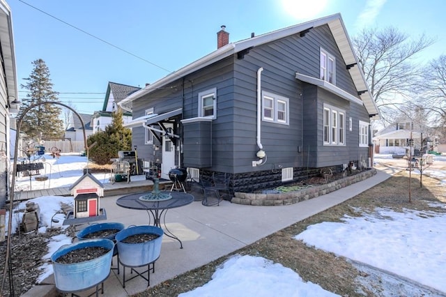 view of snowy exterior with a chimney, a patio area, and fence