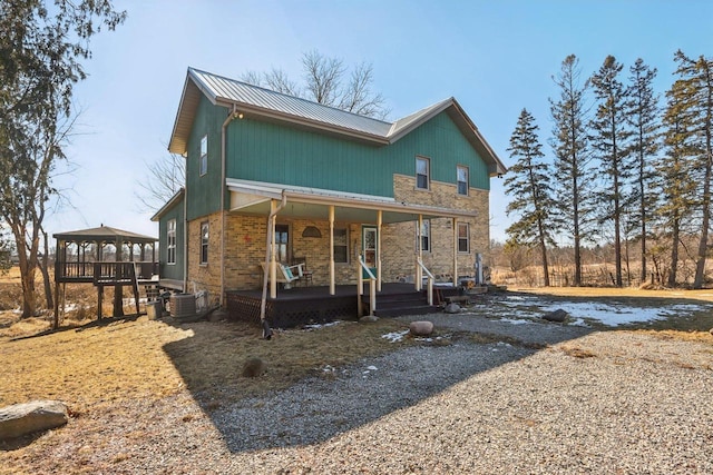 view of front of house featuring metal roof, covered porch, brick siding, driveway, and a gazebo