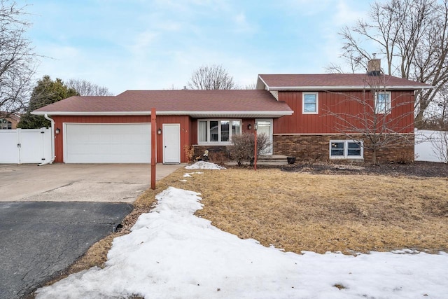 split level home with an attached garage, brick siding, fence, driveway, and a chimney