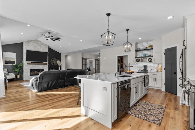 kitchen with a fireplace, a sink, white cabinetry, vaulted ceiling, and dishwasher