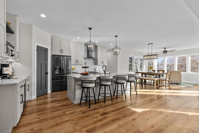 kitchen with a breakfast bar, tasteful backsplash, white cabinets, fridge with ice dispenser, and light wood-type flooring