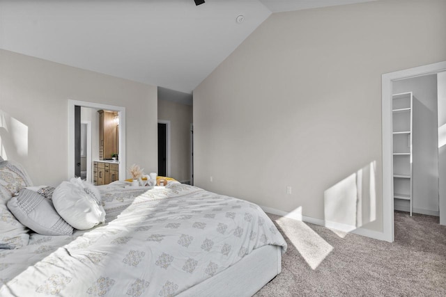 carpeted bedroom featuring vaulted ceiling, ensuite bathroom, a walk in closet, and baseboards